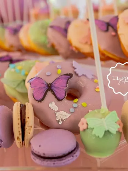 An assortment of beautifully decorated donuts, macarons, and cake pops in the party's soft pastel color palette.
