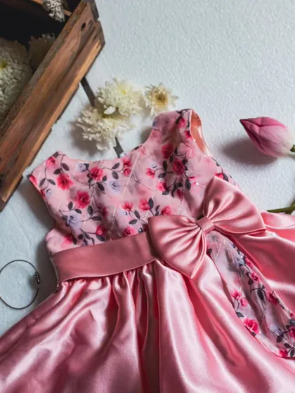 A beautiful flat lay of a peach satin dress. This angle showcases the sheen of the fabric, the floral embroidered bodice, and the elegant drape of the bow.
