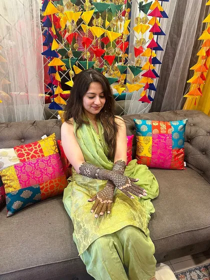 A candid moment of a client enjoying her mehndi function, her intricate hand and arm designs complementing her green outfit.