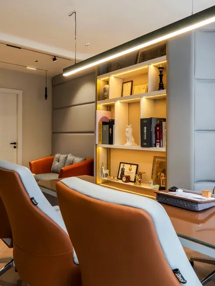 Another director's cabin, featuring fabric-paneled walls and modern orange chairs. The linear pendant light and built-in shelving create a space that is functional, stylish, and personalized.