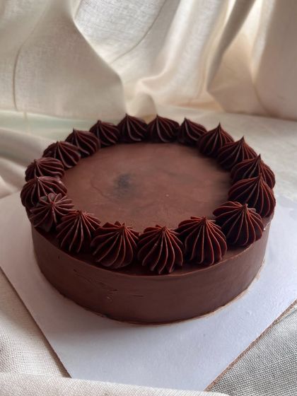A classic 6-inch eggless chocolate cake. It's a rich chocolate sponge covered entirely in smooth, dark chocolate ganache with a simple piped border.