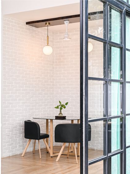 The same dining nook, but with the warm pendant light turned on. The lighting enhances the texture of the white brick wall and creates a cozy, inviting ambiance perfect for conversation.
