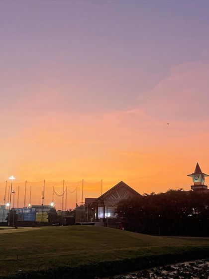 The sky glows with color over the driving range at dusk. My coaching sessions can be scheduled for various times, including evening practice under the lights.