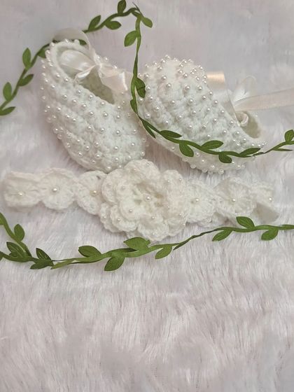 A simple and elegant set for a baby girl. The white beaded booties and matching floral headband are styled with a green vine to highlight their delicate, nature-inspired design.