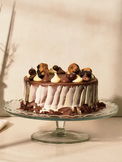 The full Chocolate Heaven cake on a glass stand, ready to be served. The combination of dark and white chocolate makes it visually striking.