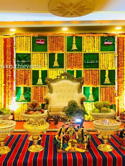 A traditional Seemantha setup with a checkerboard backdrop and striped floor mat. The stage is decorated with offering trays, traditional dolls, and brass lamps, reflecting our rich cultural heritage.