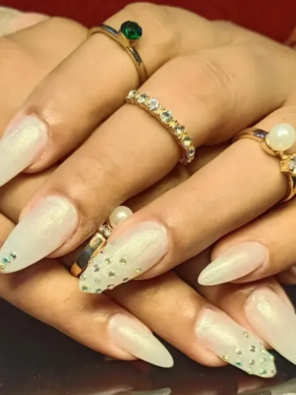 A beautiful set of pearly white stiletto nails with accent nails featuring a cascade of sparkling rhinestones.