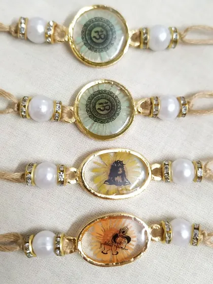 This collection of spiritual rakhis includes designs with the sacred 'Om' symbol and images of Lord Shiva. Each one is set in resin with a floral background, attached to a simple thread with pearl and crystal beads.