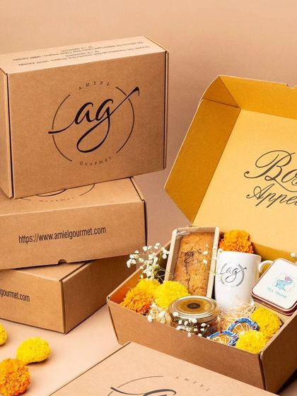 A beautifully arranged Diwali hamper, ready for gifting. This box is filled with festive treats, including a tea cake, cookies in a jar, an AG mug, and decorated with marigold flowers.