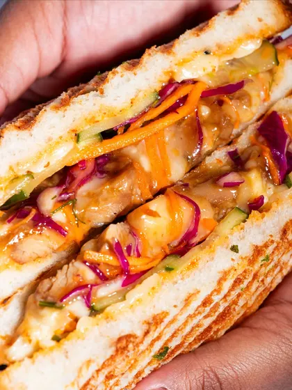 A detailed cross-section of the Togarashi Chicken Melt, revealing the colourful slaw, tender chicken, and melted cheese.
