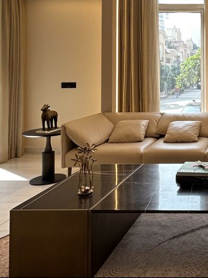 Sunlight streams into the living room, highlighting the textures of the plush leather sofa and the dark marble coffee table. We prioritize natural light in our designs to create bright and uplifting living environments.