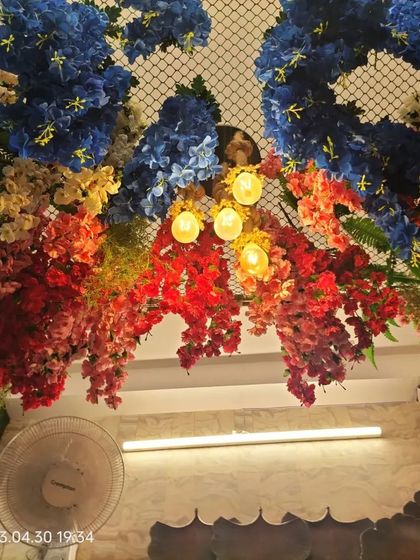 Looking directly up at the floral ceiling installation. The combination of bright flowers and warm lights creates a joyful and immersive experience for anyone standing underneath.