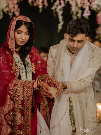 A groom and bride during their wedding ceremony. His sherwani, crafted with over 80 hours of hand embroidery, features soft hues of cream and pink inspired by Koyalia birds, reflecting the venue's tranquil beauty.