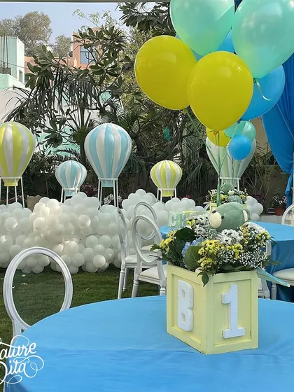 A close-up of the table setting, featuring a centerpiece with a teddy bear and balloons, and a backdrop of hot air balloon props nestled in 'clouds' of white balloons.