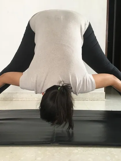 This student is in the fourth variation of Prasaritha Padottanasana, holding the ankles to deepen the forward bend and inversion.