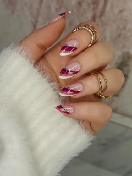 An elegant and artistic French manicure with abstract burgundy and gold-lined tips. The combination of rich color and metallic detail creates a luxurious and sophisticated look.