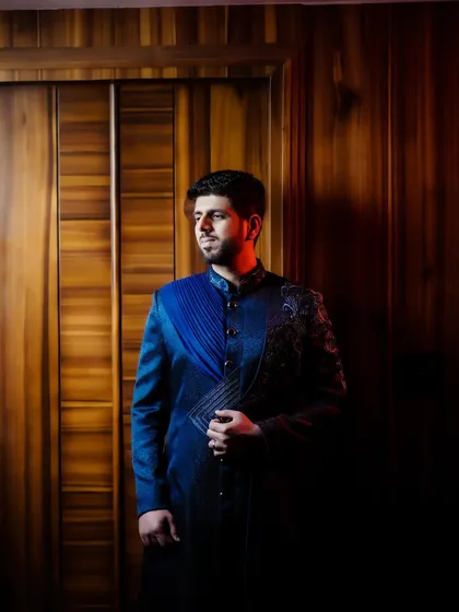 A dramatic, low-light portrait of the groom in his stylish reception sherwani, using shadows to create a powerful image.