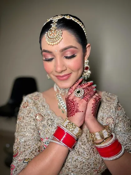 A moment of quiet reflection. The soft lighting highlights the flawless finish of the makeup and the intricate details of her bridal attire.