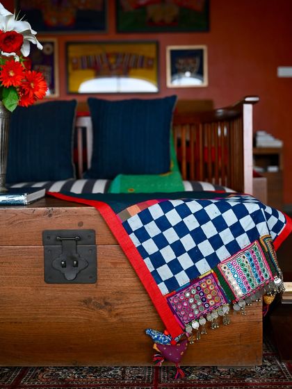 A close-up of the throw draped over a wooden chest. You can see the detailed embroidery, mirror work, and old coins that make each Lambani patch a small work of art.