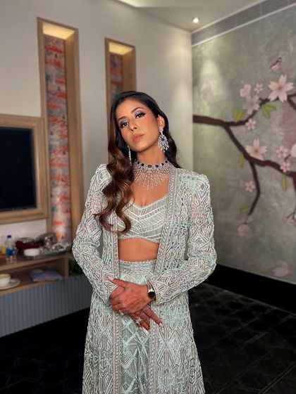 A full-length view of this powerful cocktail look. The makeup is designed to be striking and confident, holding its own with the intricate details of the designer outfit.