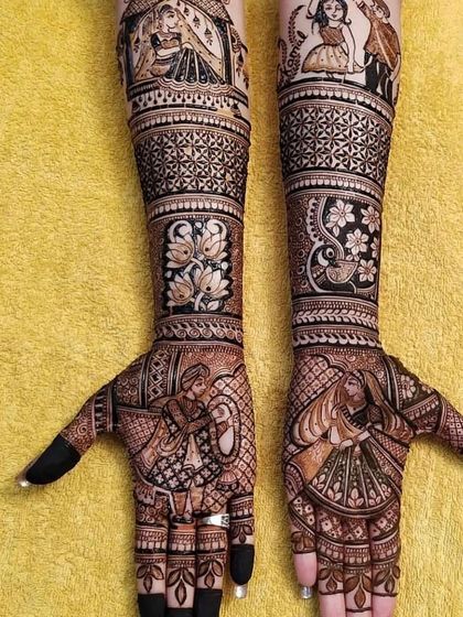 This design tells a complete wedding story. It includes portraits of the couple during the varmala ceremony on the palms, with other figures and floral patterns extending up the arms.