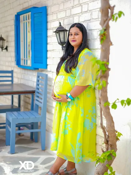 A lovely solo portrait of the mother-to-be in a casual yet elegant dress against a white brick wall.