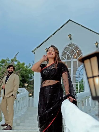 An elegant pre-wedding portrait on a white bridge. The bride's black saree stands out beautifully against the classic architecture, creating a timeless and sophisticated look.