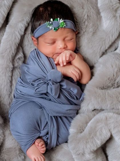 This portrait showcases the beauty of a simple swaddle on a plush, textured blanket. The focus is entirely on the baby's tiny, curled-up form and delicate features, like her little hand resting on her cheek.