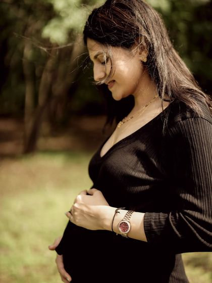 A beautiful, warm-toned solo portrait of the mom-to-be in a forest setting, looking down at her bump with a gentle smile.