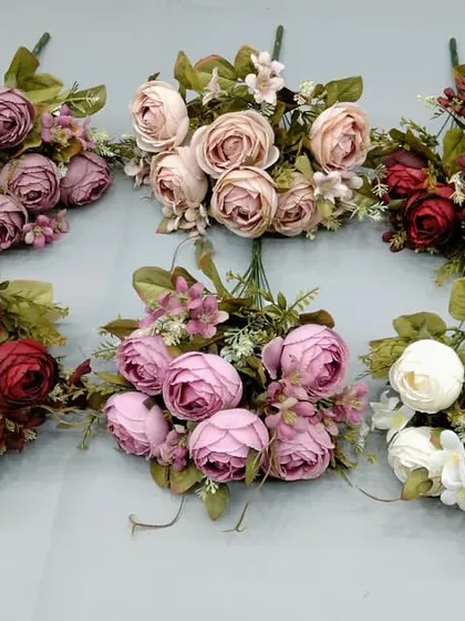 A selection of artificial ranunculus and rose bunches in various vintage-inspired colors like mauve, dusty rose, and deep red.