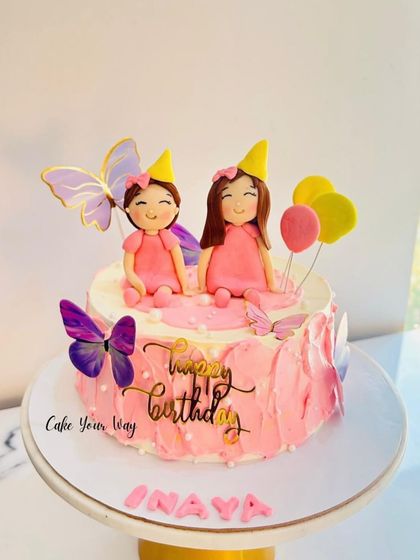Double the sweetness with this cake for twins. Featuring two adorable fondant figures, balloons, and butterflies, it's a perfect celebration of togetherness.