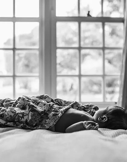 A black and white photo of a newborn sleeping on a bed, with a window in the background. This artistic shot creates a timeless and emotional feel.