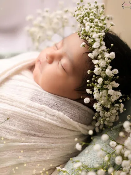 A detailed close-up of a newborn's face, adorned with a crown of fresh baby's breath. This macro shot captures the delicate skin, tiny eyelashes, and serene expression of a sleeping baby.