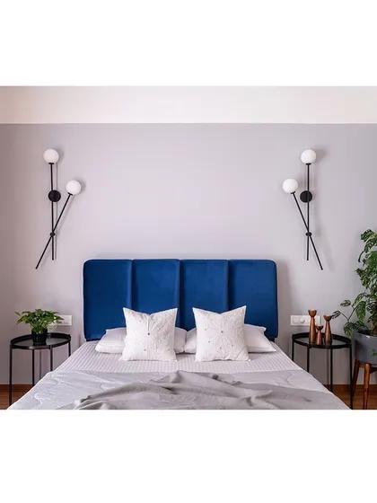 This bedroom features a symmetrical design with a deep blue headboard and modern globe sconces. The simplicity of the arrangement creates a calm and balanced feeling.