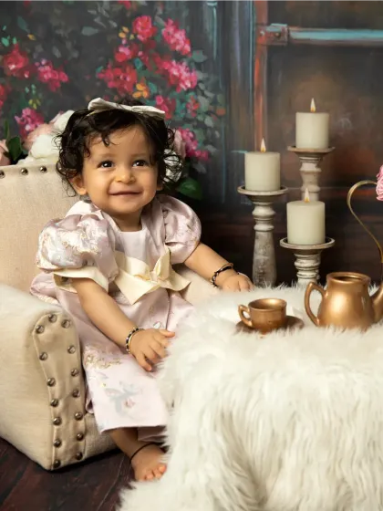 A bright, happy smile from this little girl at her tea party. The candlelight and floral background add a touch of magic to the scene.