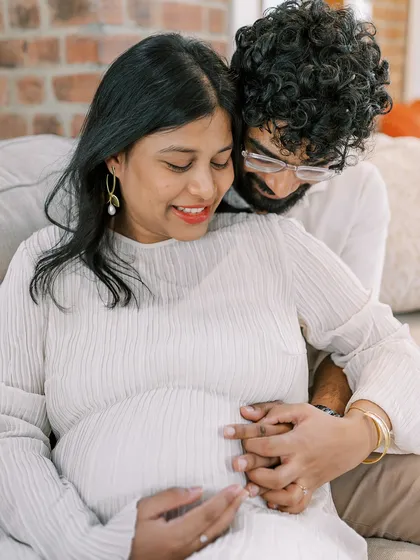 A close-up showing the partner's hands gently holding the baby bump. This simple gesture is so full of love and protection, a beautiful detail to capture during a home maternity session.