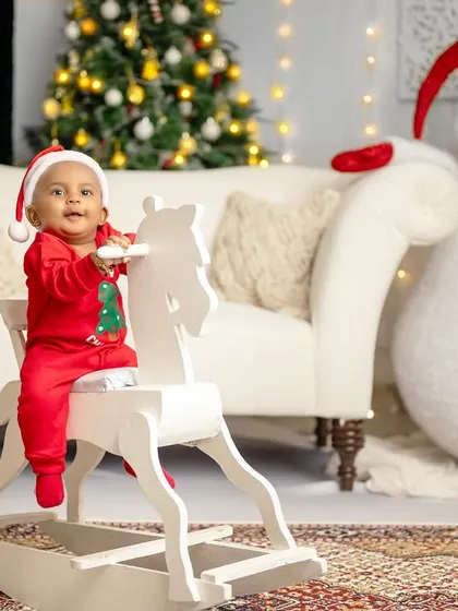 A little boy in a festive red outfit sits happily on a rocking horse, ready to ride into the Christmas celebrations.