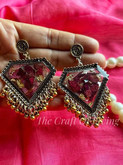 A pair of diamond-shaped, silver-toned earrings with preserved red petals. The mix of silver and gold accents gives these earrings a modern, edgy look.