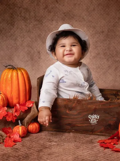 The cutest pumpkin in the patch! A happy baby sits in a wooden crate, surrounded by autumn leaves and pumpkins.