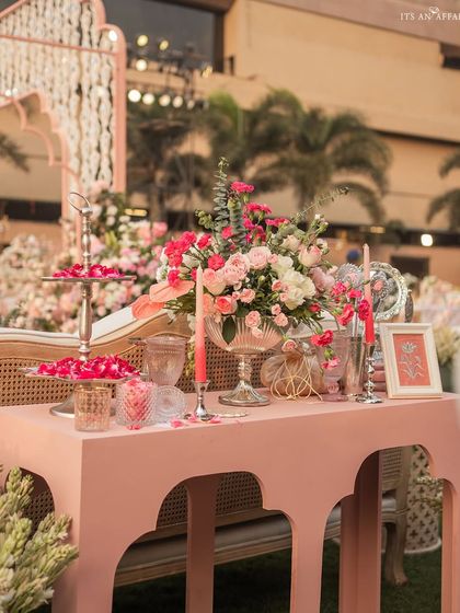 A console table decorated with a lush floral centerpiece, pink candles, and elegant glassware.