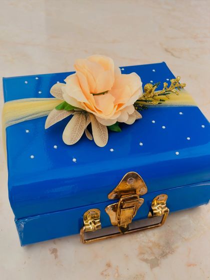 The exterior of a handcrafted bridal hamper. This elegant blue trunk is decorated with a delicate flower, ready to be filled with love, joy, and a little sparkle for the bride.