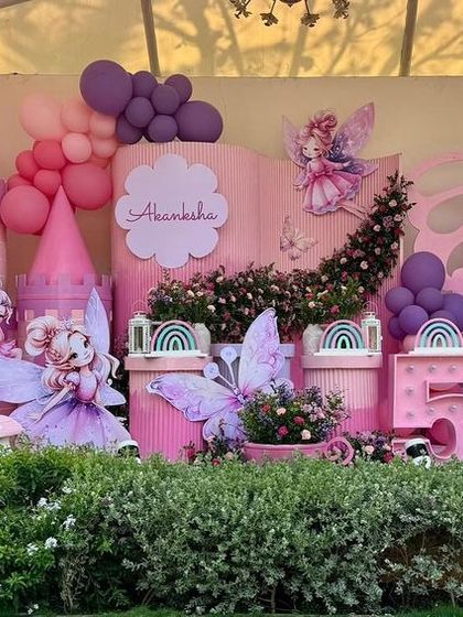 An enchanting fairy land created for a 5th birthday, with a pink castle, whimsical fairy cutouts, and floral decorations. The entire scene is set in a garden to enhance the magical, outdoor feel.