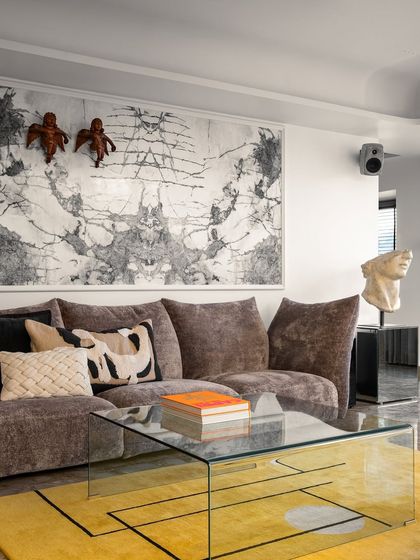 A closer look at the art-filled living space, where a plush sofa and glass coffee table sit atop a vibrant yellow rug. The room is a gallery of personal taste, designed to be both inspiring and deeply comfortable.