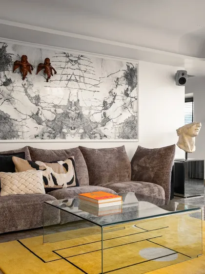 A closer look at the art-filled living space, where a plush sofa and glass coffee table sit atop a vibrant yellow rug. The room is a gallery of personal taste, designed to be both inspiring and deeply comfortable.
