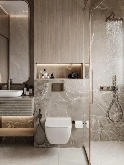 I transform bathrooms into personal spa-like retreats. This design features large-format marble-look tiles, wood-finish cabinetry for warmth, and a glass-partitioned walk-in shower with a rain shower head. The backlit mirror and built-in storage niche add both function and a touch of luxury.