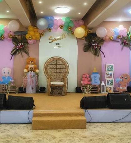 This wide shot showcases the complete stage setup for a teddy bear themed baby shower in a banquet hall. The colorful balloon arch and themed props create an impressive focal point for the celebration.