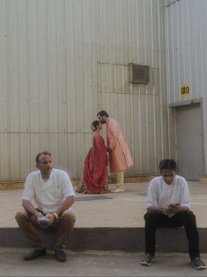 An unconventional, documentary-style shot of the couple kissing in the background while two men sit in the foreground. This image tells a story of love existing in the real, unfiltered world.