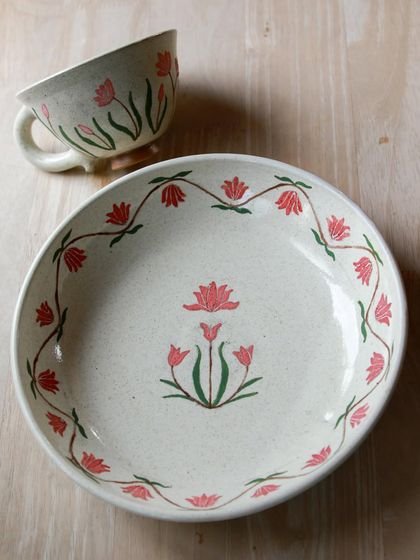 A beautifully hand painted plate and footed cup with delicate pink and green floral patterns, created by a student during their course.