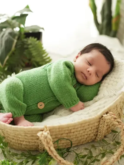 A side profile of a sleeping newborn in a green knit romper, showing the delicate features of the baby. We pay close attention to posing and lighting to create artistic portraits.