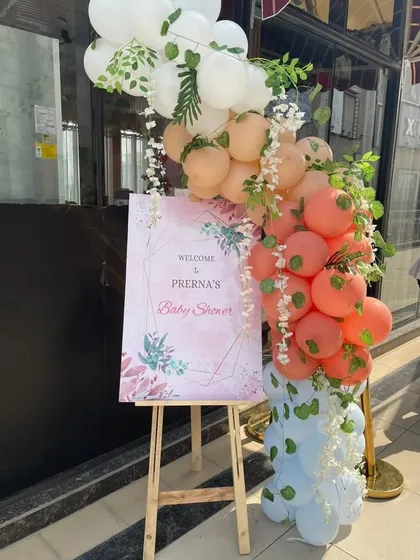 A welcome easel for a baby shower, decorated with a beautiful balloon garland in pastel colors.